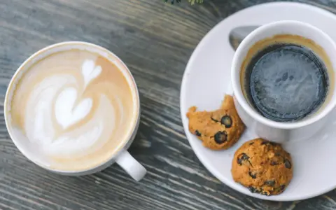 Zwei Tassen Kaffee: ein Latte mit Herz und ein starker Americano mit Keksen.