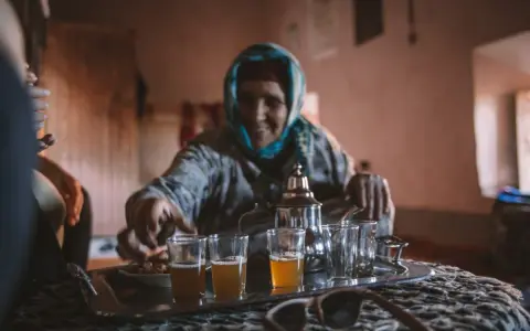Maroko: starsza kobi nalewa herbatę miętową do szklanek. W tle widać tradycyjny wystrój.