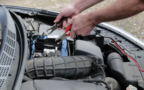 Ręce podłączają kable do akumulatora, bo auto nie odpala.