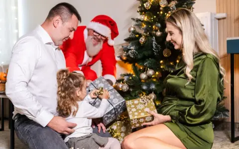 Rodzina otwiera prezenty przy choince, a Mikołaj uśmiecha się w tle. Wesołe święta w hotelu.