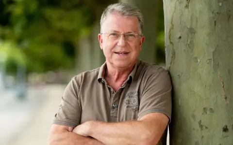Carsten Sostmeier, ein Mann mit Brille und grauem Haar, lehnt lächelnd an einem Baum.