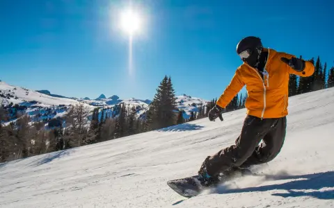 Snowboardzista w pomarańczowej kurtce zjeżdża po stoku, unosząc śnieg. To świetny przykład, jak jeździć na snowboardzie.