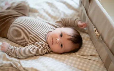 En 1 månads bebis sover inte, utan ligger vaken på en rutig filt i en säng.