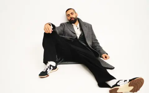 Ardalan Esmaili sitter avslappnat i en grå rock, vit skjorta och svarta byxor. Hans sneakers har en unik design.