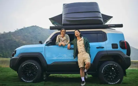 Coppia sorridente accanto a un toyota land cruiser mini blu, pronto per l'avventura con tettoia e box sul tetto.