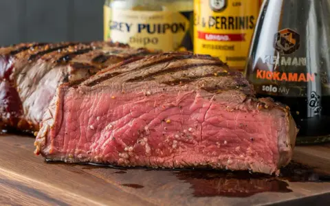 Saftiges, medium-gebratenes Steak mit Grillstreifen, daneben Flaschen für die perfekte Steak Marinade.