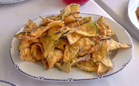 Montón de berenjenas fritas crujientes y doradas en un plato blanco con borde azul. ¡Un aperitivo delicioso!