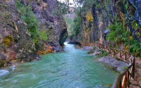 Un río turquesa serpentea entre cañones rocosos, con un sendero de madera que acompaña el recorrido. Ideales para rutas senderismo Jaén.