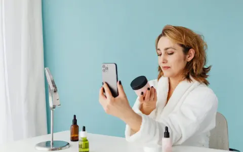 Kobieta w szlafroku sprawdza oryginalność kosmetyku za pomocą aplikacji na telefonie.