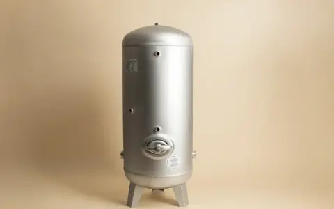 En silverfärgad hydrofor eller hydropress står på tre ben mot en ljusbeige bakgrund.