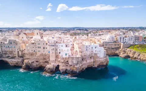 Vista aerea di Polignano a Mare, una delle più belle città da visitare in Puglia, con case bianche aggrappate alle scogliere a picco sul mare turchese.