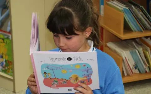 Niña leyendo un libro ilustrado, parte de una colección de libros por edades.