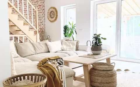 Jasny salon w stylu boho z beżową kanapą, drewnianymi schodami i ceglaną ścianą.