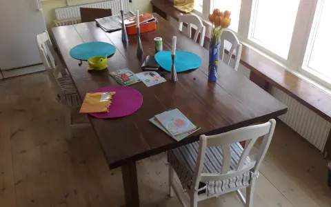 Ett gammalt furubord med stolar, dukar, ljus och en vas med tulpaner.