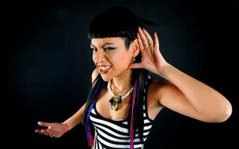 Fatima Hajji, con su característico estilo, escucha atentamente, con una mano en la oreja y una sonrisa pícara.