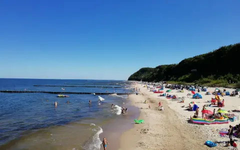 Sonniger Tag am Strand Koserow mit vielen Badegästen, bunten Sonnenschirmen und spielenden Kindern im flachen Wasser.