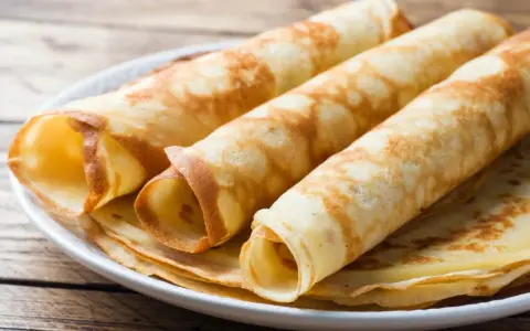 Gestapelte, gerollte Pfannkuchen ohne Mehl auf einem Teller. Sie sind goldbraun und sehen lecker aus.