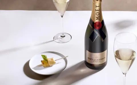 Moët & Chandon Champagnerflasche neben einem Glas Champagner und einem kleinen Häppchen. Das Etikett zeigt das Gründungsjahr, was auf den Degorgierdatum Champagner hinweist.