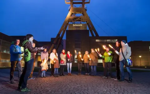 Eine Gruppe von Menschen hält nachts Fackeln vor dem Förderturm der Zeche Zollverein.