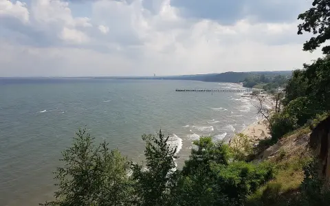 Widok z klifu orłowskiego na morze, plażę z ludźmi i molo. W oddali widać zarys wybrzeża.