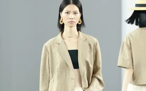 Ein Model trägt einen beigen Blazer aus knitterndem Leinen mit einem schwarzen Top. Große, runde Ohrringe schmücken ihre Ohren.