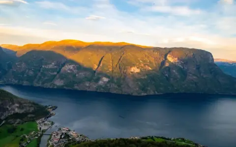 En vy över Sognefjorden med solbelysta berg och en liten by vid vattnet. Som en levande sognefjorden karta.