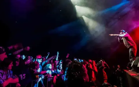 Raper na scenie, w świetle reflektorów, wskazuje palcem na tłum. Koncert w **3 wymiar**ze, pełen energii i emocji.