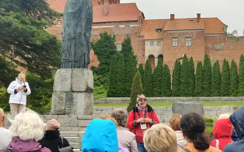 Grupa turystów słucha przewodnika przy pomniku Kopernika. To jedna z wielu atrakcji Warmii, gdzie historia ożywa.