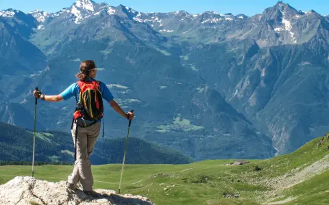 Donna con zaino e bastoncini da trekking ammira i maestosi **sentieri Valle d'Aosta** e le cime innevate.