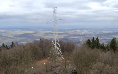 Wielki metalowy krzyż góruje nad lasem na Chełmcu. W dole rozciąga się panorama miasta i pagórkowatego krajobrazu.