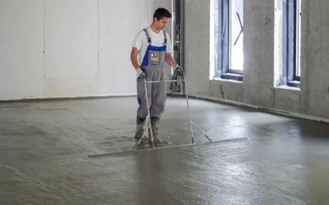 Pracownik wyrównuje świeżą wylewkę betonową na styropianie, dbając o jej minimalną grubość.