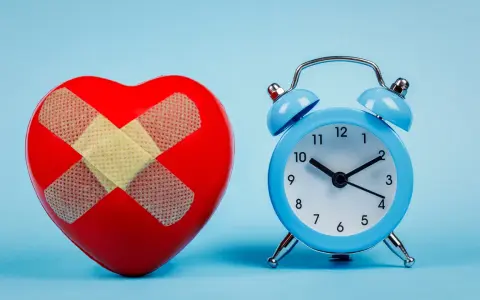 Rotes Herz mit Pflastern und blauer Wecker. Wenn du eine schlaflose Nacht hast, was tun? Zeit für Heilung.
