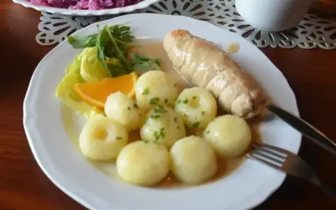 Pyszne kluski śląskie z roladą mięsną, surówką z czerwonej kapusty i plasterkiem pomarańczy.