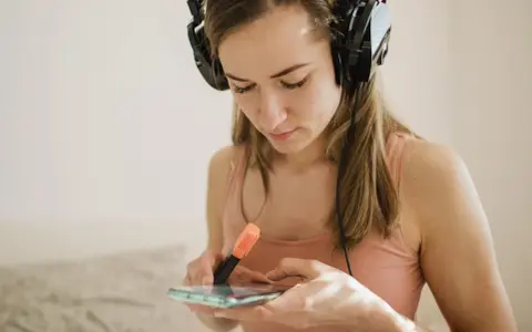 Dziewczyna w słuchawkach przegląda spotify lyrics na telefonie, zaznaczając fragmenty pomarańczowym pisakiem.