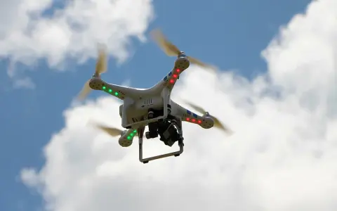 Weiße Drohne mit roten und grünen Lichtern fliegt im blauen Himmel mit Wolken. Beachten Sie die Drohnen Richtlinien für sicheren Flug.