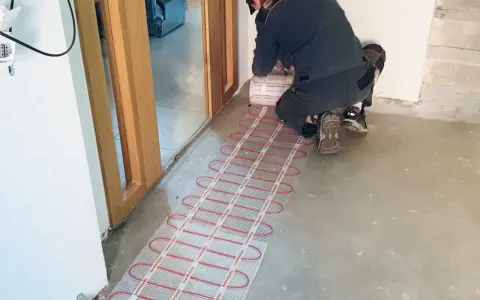 Instalator montuje matę grzewczą, przygotowując ogrzewanie elektryczne podłogi.