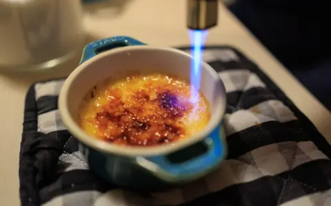 Flamme bleue caramélisant le sucre d'une crème brûlée, rappelant son origine.