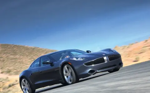 Elegancki, ciemnoszary Fisker Karma sunie po pustynnej drodze pod błękitnym niebem.