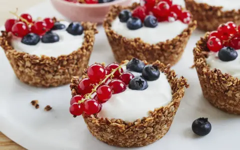 Leckere Granola Cups gefüllt mit Joghurt und garniert mit roten Johannisbeeren und Blaubeeren.