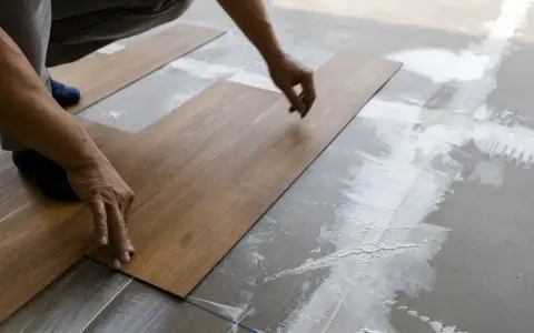 Hände legen Holzoptik-Vinylboden auf Kleber. Das Verlegen von Vinylboden erfordert Präzision.