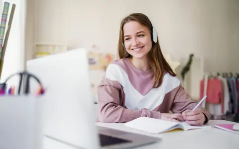Uśmiechnięta dziewczyna w słuchawkach uczy się do matury. Szuka inspiracji do pisania opinion essay matura tematy.