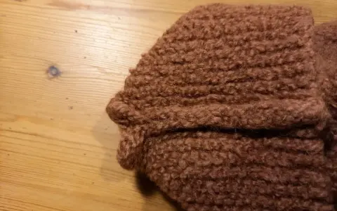Bruna, sticka tovade tofflor ligger på ett träbord.