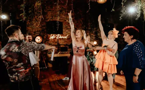 Wesele w pełni! Neon "Let's Dance!" i kobiety w sukniach unoszą ręce. Świetny pomysł na oczepiny i zabawę do białego rana.