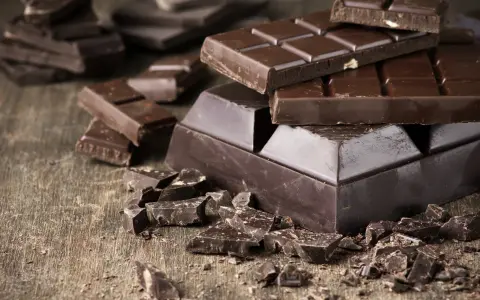 Des morceaux de chocolat noir, entiers et brisés, sur une table en bois. Une invitation à découvrir comment adoucir le chocolat noir pour une dégustation parfaite.