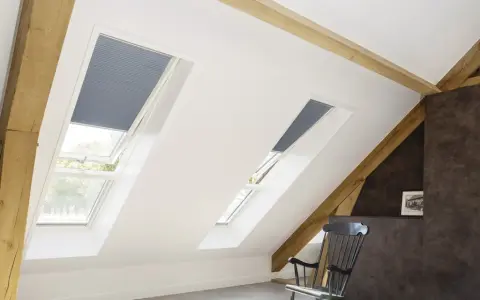 Schicke Dachfenster mit Plissees verkleiden. Holzbalken und ein gemütlicher Schaukelstuhl schaffen eine warme Atmosphäre.
