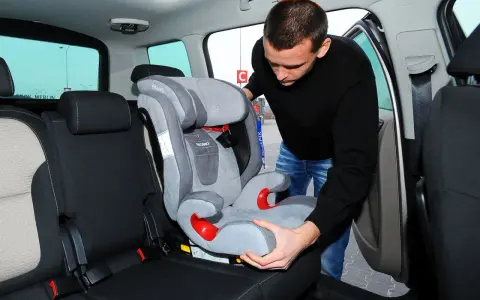 Mężczyzna montuje fotelik dziecięcy, pokazując, jak zamontować isofix w aucie.