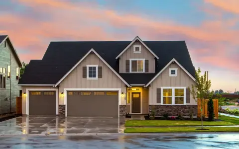 Belle maison prête à finir, prix attractif. Façade beige, toit noir, garage double, jardin verdoyant sous un ciel pastel.