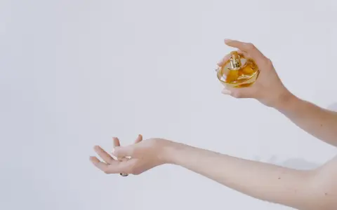 Dłoń trzymająca perfumy nad drugą dłonią.