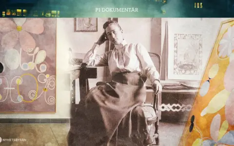 En kvinna sitter vid ett skrivbord, omgiven av färgstarka hilma af klint-konstverk.