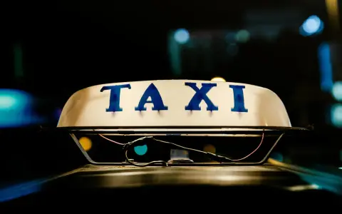Tetto di un taxi con la scritta "TAXI" in blu. La luce soffusa e i riflessi suggeriscono la notte, un momento in cui ci si interroga quanto guadagnano i tassisti.